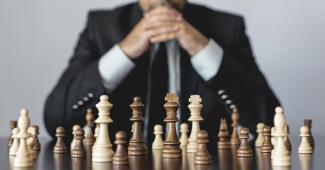 A person in a suit sitting behind a chessboard with their hands together in a "ready to play" position.